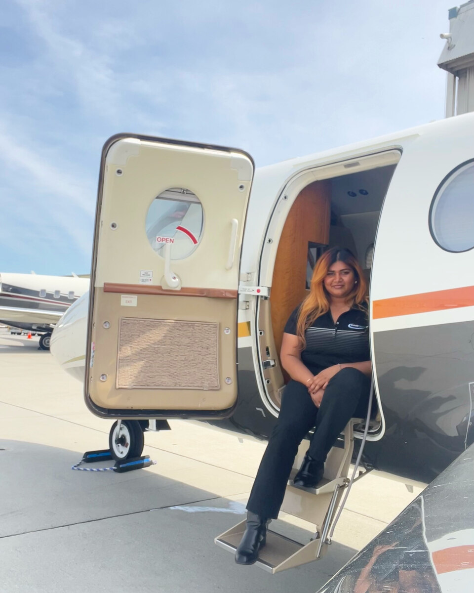 Petrriann De Bond sits on the entry steps of a business aircraft parked on the ramp.